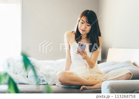 ベッドでスマートフォンを使う笑顔の女性 ベッドでスマートフォンを使う笑顔の女性 113268758