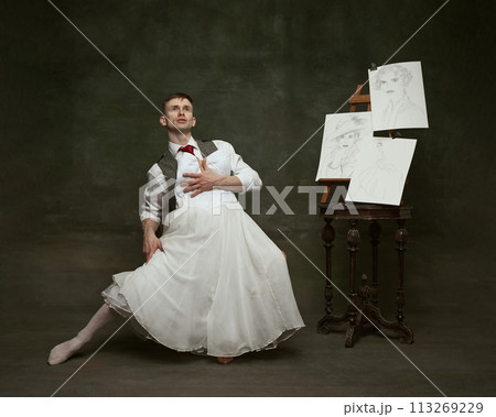 Portrait of handsome man dressed in vintage formal suit and holding white woman's dress fitting in his hands. Self-expression. Portrait of handsome man dressed in vintage formal suit and holding white woman's dress fitting in his hands. Self-expression. 113269229