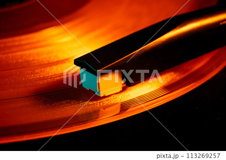 Close-up photo of turntable needle on vinyl record with warm orange glow. Vintage things. Close-up photo of turntable needle on vinyl record with warm orange glow. Vintage things. 113269257