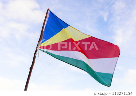 Flag of Seychelles waving in wind under cloudy blue sky on a sunny day 113271154