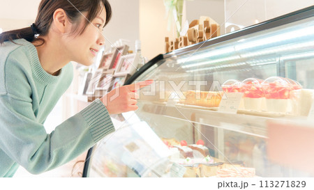 ショーウィンドウ内のケーキを選ぶ若い女性 ショーウィンドウ内のケーキを選ぶ若い女性 113271829