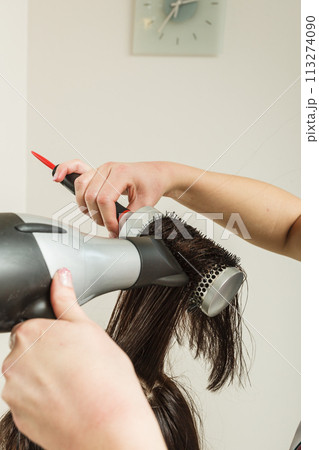Hairdresser drying dark female hair using professional hairdryer Hairdresser drying dark female hair using professional hairdryer 113274090