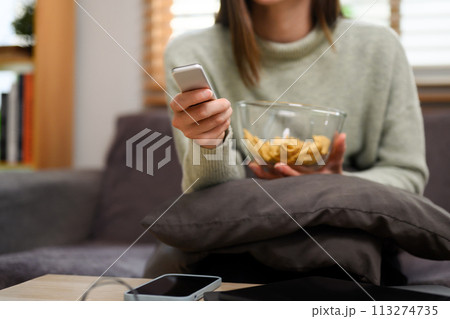 Cropped shot of young woman with remote control in hand watching TV in living room 113274735