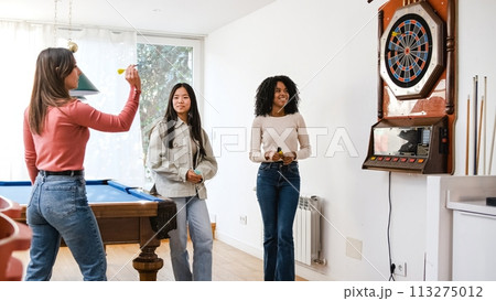 Happy diverse female friends playing dart in game room at home Happy diverse female friends playing dart in game room at home 113275012