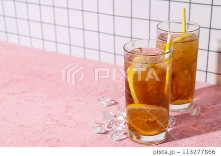 A glass of cold tea with ice and an orange on a pink background A glass of cold tea with ice and an orange on a pink background 113277866