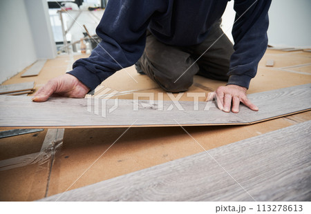 Close up of man hands laying laminate wooden planks on the floor in apartment under renovation. Male construction worker installing timber laminate flooring at home. Hardwood floor renovation concept. Close up of man hands laying laminate wooden planks on the floor in apartment under renovation. Male construction worker installing timber laminate flooring at home. Hardwood floor renovation concept. 113278613