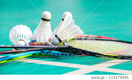 White badminton shuttlecocks and badminton rackets on green floor indoor badminton court soft and selective focus on shuttlecocks and the rackets 113279585