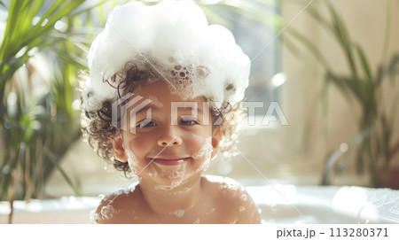 Adorable child with a bubbly hairdo beams in a bath, bringing joy and splashes of fun 113280371