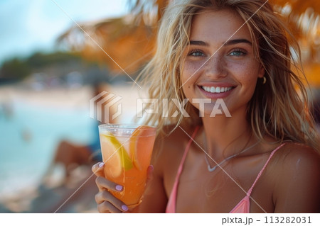 Sexy girl drinks a bright cocktail. Bright pink swimsuit, beach background. Smile and look at the camera. 113282031