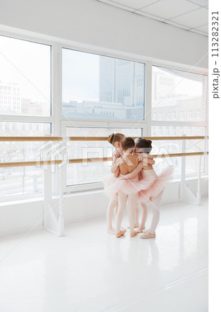 Cute little girls, ballerinas hugs in group while training near barre in light modern dance studio. Classical ballet school. 113282321
