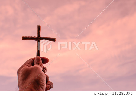 His left-hand holding cross up to the golden yellow sky. Left copyspace for entering text. Close-up shot with blurry clouds on a fine day. 113282370