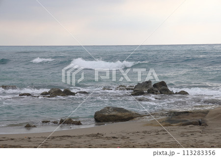 A lone figure in front of foam waves and a historic mountain in Alanya, November 2021. 113283356
