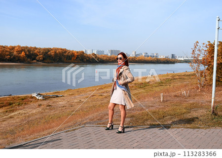 a confident young attractive woman in a coat and high-heeled shoes walks through the streets of the city, the woman smiles and enjoys life a confident young attractive woman in a coat and high-heeled shoes walks through the streets of the city, the woman smiles and enjoys life 113283366