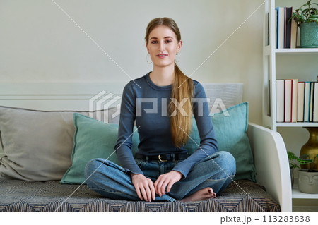 Portrait relaxed teenage girl sitting in lotus position on couch at home Portrait relaxed teenage girl sitting in lotus position on couch at home 113283838