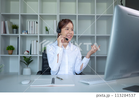 Portrait of happy smiling female customer support phone operator at workplace. Asian Portrait of happy smiling female customer support phone operator at workplace. Asian 113284537