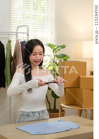 Young business woman takes a photo of a cloth with her smartphone device to put it up for sale on a second-hand clothing platform. online selling concept 113284592