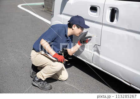 傷ついた車の修理の見積もりをする作業員 傷ついた車の修理の見積もりをする作業員 113285267