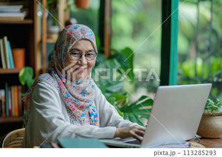 Middle aged Asian woman in hijab in front of a laptop at modern workplace Middle aged Asian woman in hijab in front of a laptop at modern workplace 113285293
