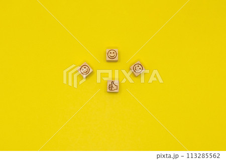 サムズアップのマークのブロックの周りに笑顔のアイコンが並ぶ黄色の背景 113285562