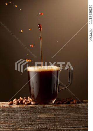 Espresso coffee glass cup with splashes on a brown background. Espresso coffee glass cup with splashes on a brown background. 113286020