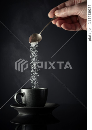 Sugar is poured into a cup of coffee. 113286022