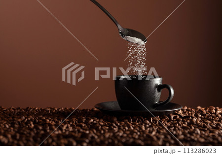 Sugar is poured into a cup of coffee. 113286023