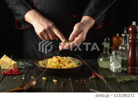 Adding aromatic spices to a bowl of pasta. The cook at the kitchen table prepares a delicious breakfast with pasta and viburnum 113286231