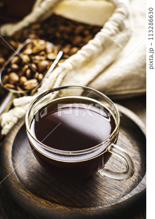 Clear cup filled with hot coffee, next to bag of coffee beans and scoop Clear cup filled with hot coffee, next to bag of coffee beans and scoop 113286630