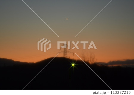 朱に染まる東の空に昇る送電線鉄塔上の明けの明星 113287219