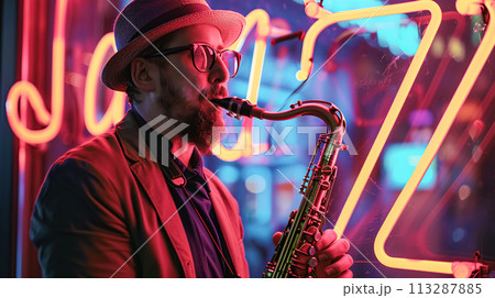 A jazz musician plays the saxophone in evening, against the backdrop of an illuminated neon "Jazz" sign. Jazz Appreciation Month, Club Life 113287885