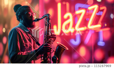 A jazz musician plays the saxophone in evening, against the backdrop of an illuminated neon "Jazz" sign. Jazz Appreciation Month, Club Life 113287969