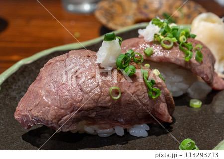 沖縄の焼物（やちむん）の黒い皿に載せられた石垣牛の握り鮨、大根おろしと小葱トッピング。 113293713