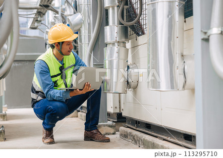 A man in a yellow vest is looking at a laptop while kneeling down. He is wearing a hard hat and safety glasses A man in a yellow vest is looking at a laptop while kneeling down. He is wearing a hard hat and safety glasses 113295710