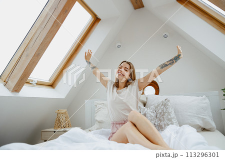 A woman is sitting on a wooden bed with her arms extended, showcasing comfort and relaxation A woman is sitting on a wooden bed with her arms extended, showcasing comfort and relaxation 113296301