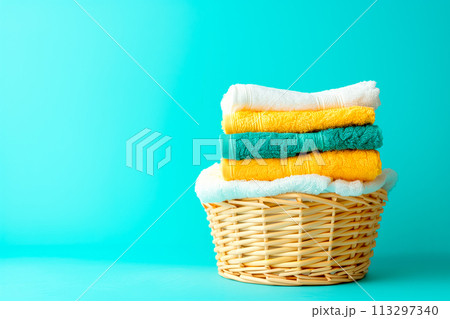 Stack of clean towels in laundry wicker basket on blue background. The towels showcasing their soft and fluffy textures Stack of clean towels in laundry wicker basket on blue background. The towels showcasing their soft and fluffy textures 113297340
