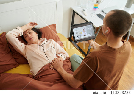 Caring husband holding hand of sick wife when video calling doctor 113298288