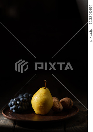 Yellow pear, blue grapes and walnuts in a clay pot on a wooden table Yellow pear, blue grapes and walnuts in a clay pot on a wooden table 113298494