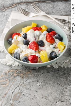 Cheesecake fruit salad with strawberries, blueberries, pineapple close-up in a bowl. Vertical 113298604