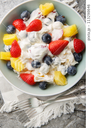 Delicious healthy cream cheese salad with strawberries, blueberries, pineapple close-up in a bowl on a marble table. Vertical top view Delicious healthy cream cheese salad with strawberries, blueberries, pineapple close-up in a bowl on a marble table. Vertical top view 113298646