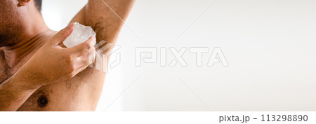 Men apply alum to their armpits to eliminate body odor after they finish showering. Alum helps deodorize men's armpits. The male hand holds alum and rubs the armpit area to eliminate the bad smell. 113298890