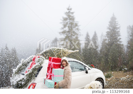 Christmas photo card of a woman with presents and car in mountains on snowy weather 113299168