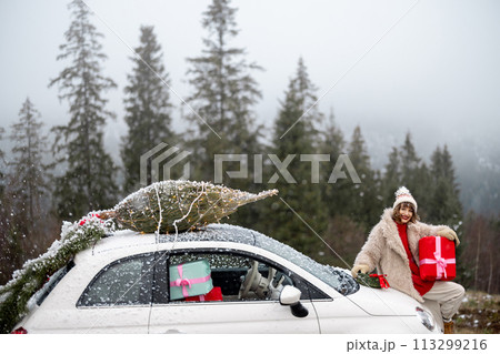 Woman travels by car with presents and Christmas tree on the mountain road Woman travels by car with presents and Christmas tree on the mountain road 113299216