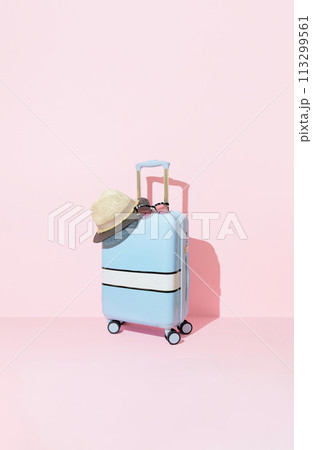 Blue suitcase with sunglasses and hat on a pastel pink background with long deep shadows. Travel concept Blue suitcase with sunglasses and hat on a pastel pink background with long deep shadows. Travel concept 113299561