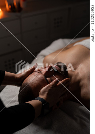 Close up shot of a professional masseuse doing face and head massage for her male client. Close up shot of a professional masseuse doing face and head massage for her male client. 113299958