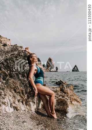 Woman beach vacation photo. A happy tourist in a blue bikini enjoying the scenic view of the sea and volcanic mountains while taking pictures to capture the memories of her travel adventure. Woman beach vacation photo. A happy tourist in a blue bikini enjoying the scenic view of the sea and volcanic mountains while taking pictures to capture the memories of her travel adventure. 113300430