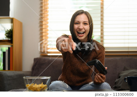 Cheerful caucasian woman with wireless gamepad having fun playing video game at home 113300600