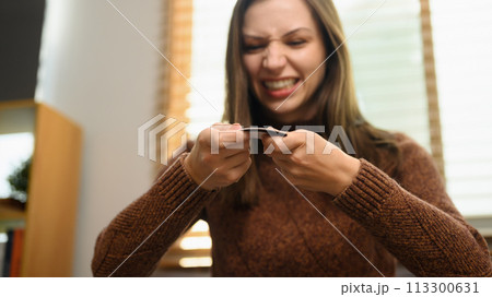 Upset young woman breaking her credit card. Financial problems concept Upset young woman breaking her credit card. Financial problems concept 113300631