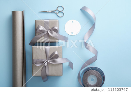 Gift wrapping. Gray paper, silver ribbon, scissors on light blue background Gift wrapping. Gray paper, silver ribbon, scissors on light blue background 113303747
