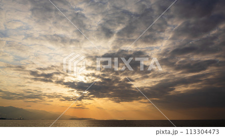 夕方の空に沈んでいく夕陽と、たくさんの雲 113304473