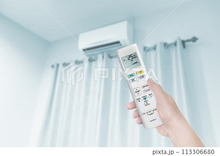 woman holding air conditioner remote control with air conditioner in blue bedroom 113306680